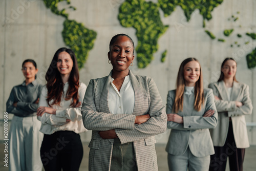 Diverse businesswomen team standing with crossed arms in front of an eco world map wall mural, representing global business and success