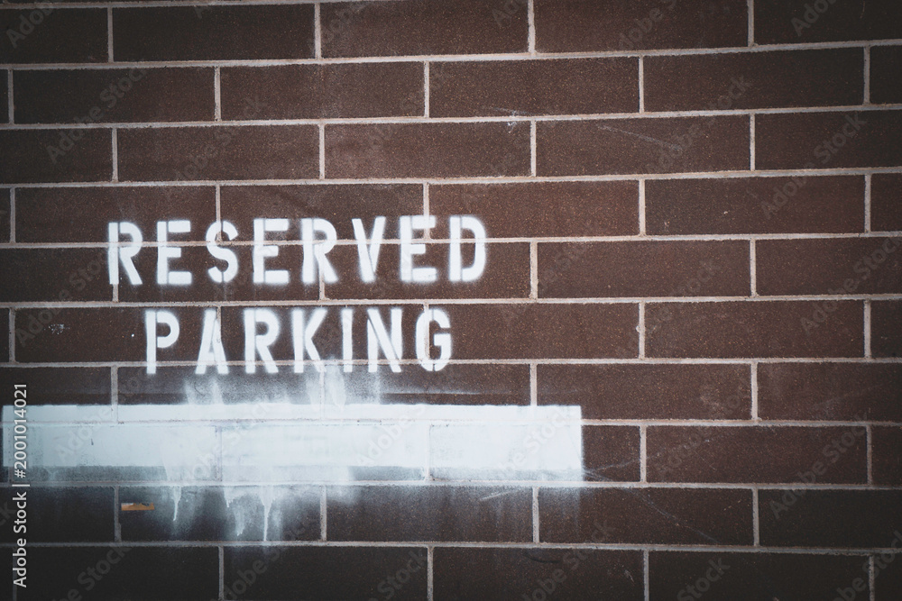 Obraz premium Reserved parking stencil sign on urban alley brick wall