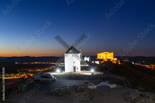White windmills and castle glowing at dusk in Consuegra, Spain