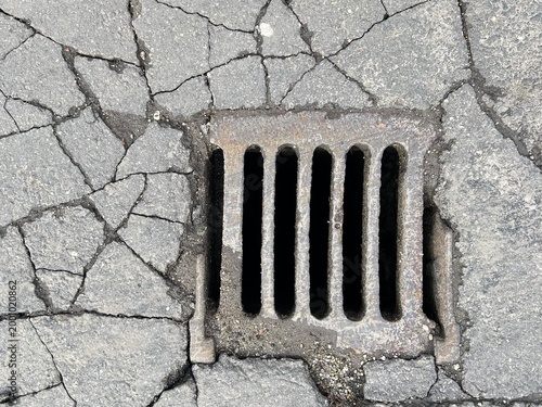 Urban surface and infrastructure texture. Frayed dusty rain water drainage at city cracked asphalt road.