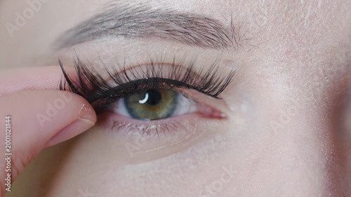 Woman puts on a false eyelashes. Young caucasian girl with green eyes, 