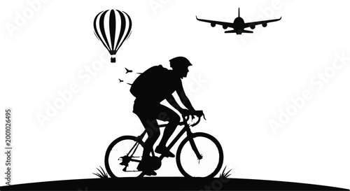 Silhouette of cyclist riding bicycle on hill with hot air balloon and airplane flying overhead in clear sky