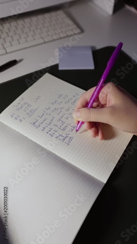 A woman sitting and writing a text into a notebook on a table at night with lamp.