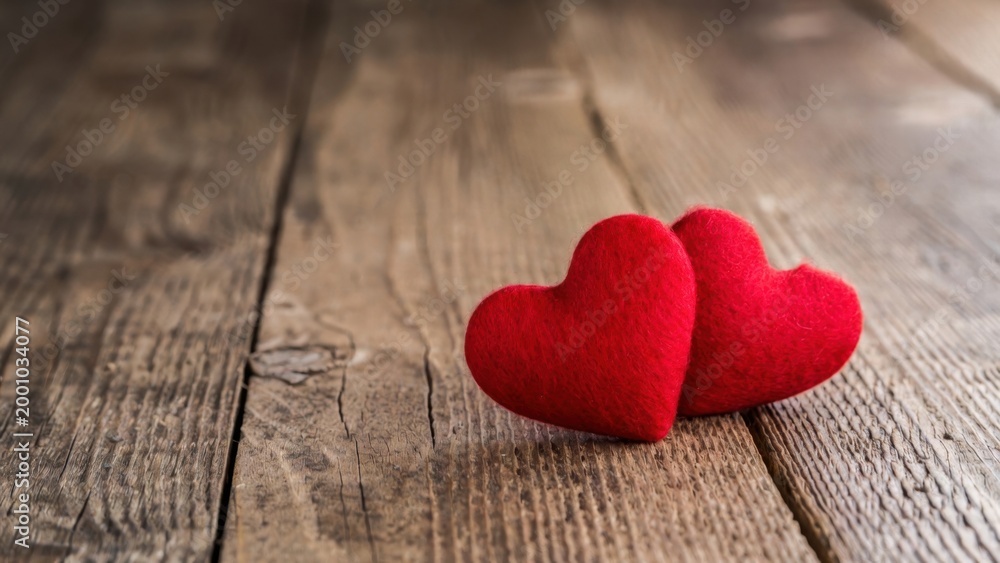 Fototapeta premium Two red hearts rest softly on weathered wooden planks