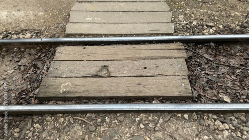 Urban surface and infrastructure texture. Close-up view of tram or train track, rails in the forest, and wooden crosswalk.