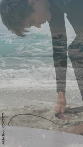 Vertical video: Surfer grabbing leash and securing plug on surfboard while waves layering frame