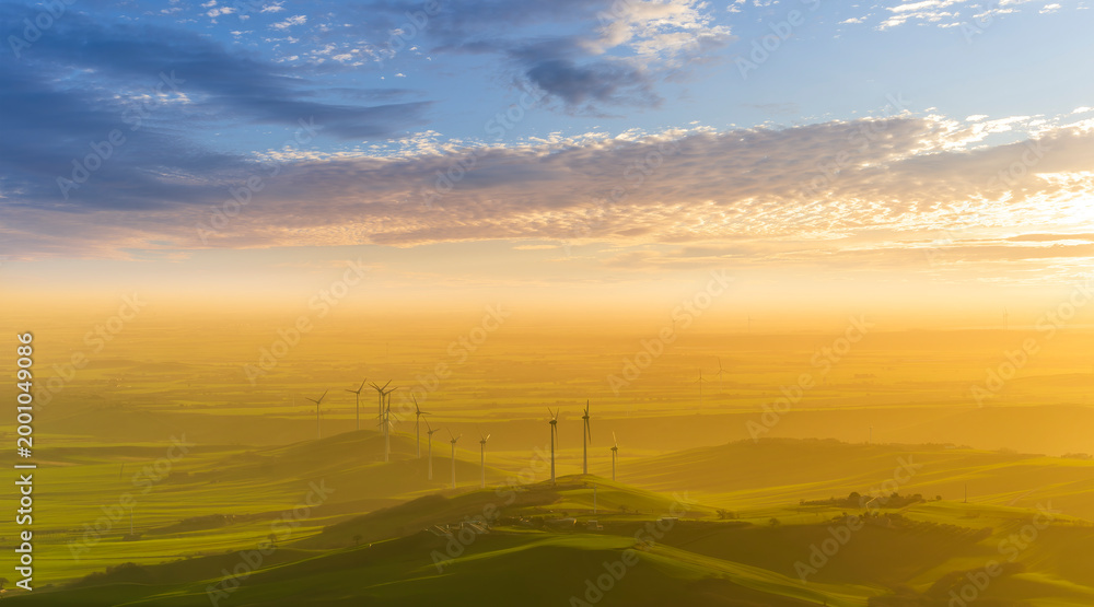 Obraz premium scenic landscape of gloden evening sunset in beautiful rural valley with amazing hills and fields and wind turbines of power plant stations with awesome clousy sky on background