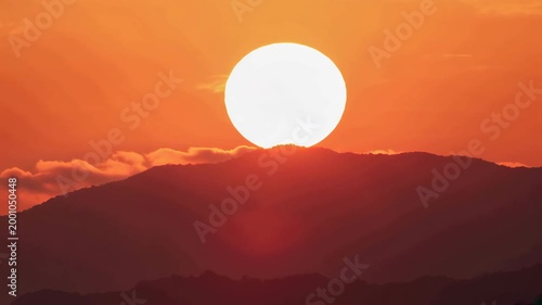 Low angle shot of sun rising above mountain peaks, illuminating the sky with warm orange hues, symbolizing a new day and natural beauty in a serene landscape