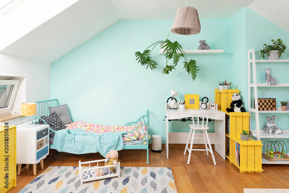 Fototapeta premium Interior of child room with bed, yellow furniture and turquoise wall. Wooden floor with design carpet. Colorful apartment in the attic.