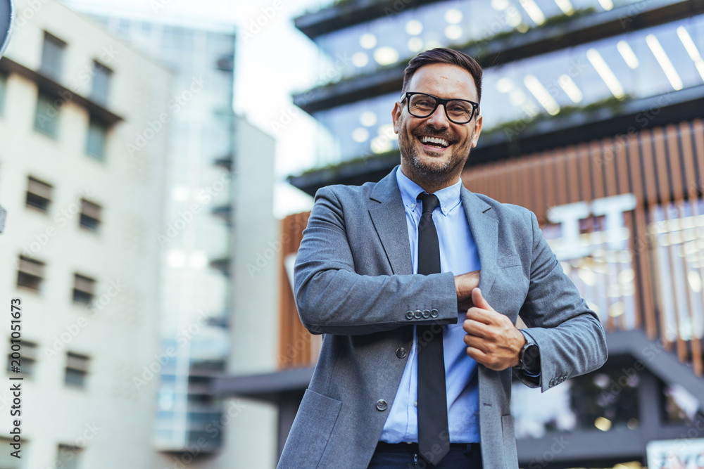 Obraz premium Confident Businessman Smiling Outdoors in Suit and Tie Near Modern Office Building