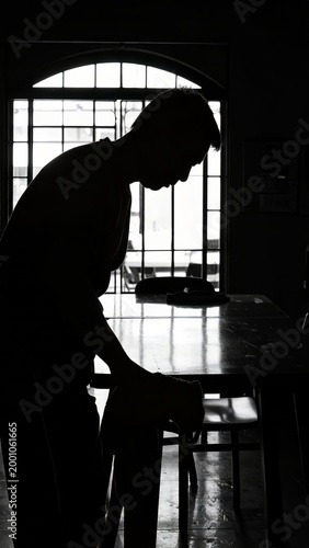Silhouette of a person standing near a table in a room with a large window