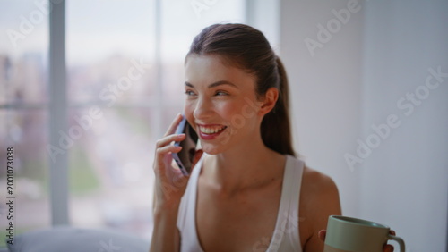 Relaxed brunette laughing cellphone sitting bed closeup. Carefree woman talking