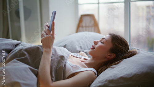 Canvastavla Awaking girl chatting smartphone in bed closeup