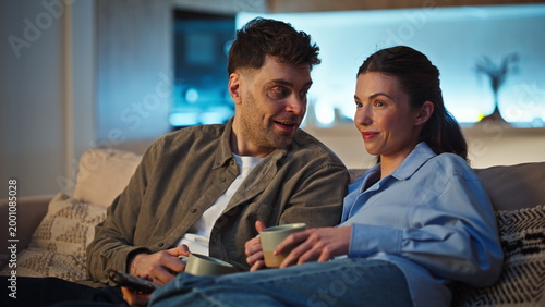 Laughing pair watching television discussing tv show domestic couch closeup