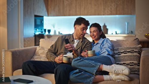 Slika na platnu Laughing couple discussing film TV at cozy apartment sofa