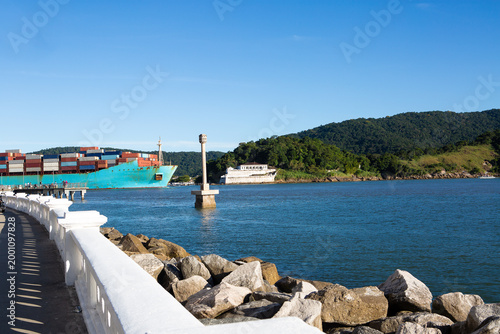 Large container cargo ship departing from the Port of Santos, the largest port in Latin America, with stacked containers and calm sea under a clear blue sky. Concept of global trade, export, import, a