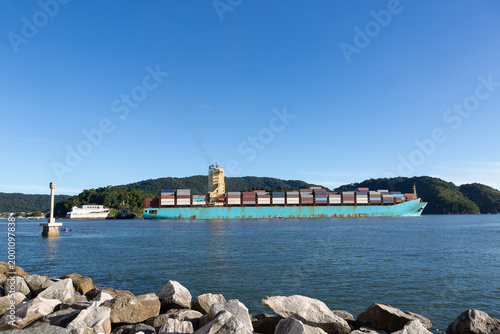 Large container cargo ship departing from the Port of Santos, the largest port in Latin America, with stacked containers and calm sea under a clear blue sky. Concept of global trade, export, import, a