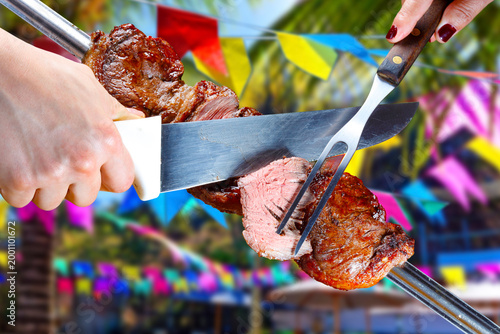 Juicy Brazilian Picanha steak on a traditional rotisserie skewer, perfectly grilled with a golden fat cap against a vibrant, festive Festa Junina background with colorful flags.