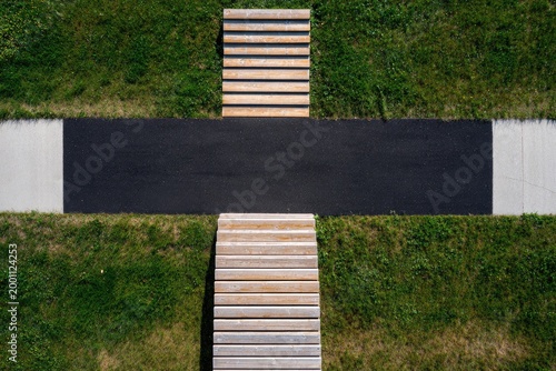 Overhead view of a modern cross-shaped pathway with wooden benches and grass