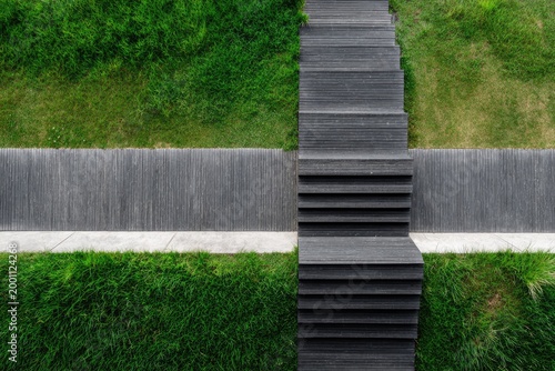 Dark wooden stairs descend through vibrant green grass and stone path