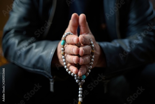 Hands clasped with prayer beads, wearing black leather jacket, close-up