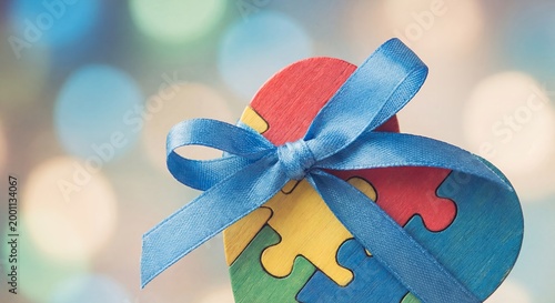 Colorful puzzle heart with blue ribbon on blurred background