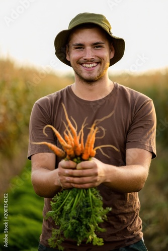 Young man holding freshly harvested carrots in a field during sunset