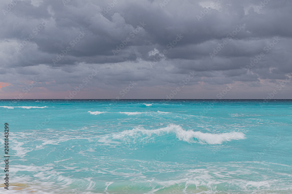 Fototapeta premium A powerful landscape showing the intense blue of the Caribbean Sea with white-capped waves under a heavy, overcast grey sky in Cancun.