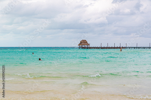 Vászonkép Tourists swim in crystal clear turquoise waters near a long pier with palapa roof on a beautiful beach in Cancun, Mexico
