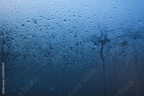 Abstract background of natural water condensation on window glass with blue gradient light. Rain drops and steam texture on transparent surface, perfect for weather, freshness, or moody concepts.