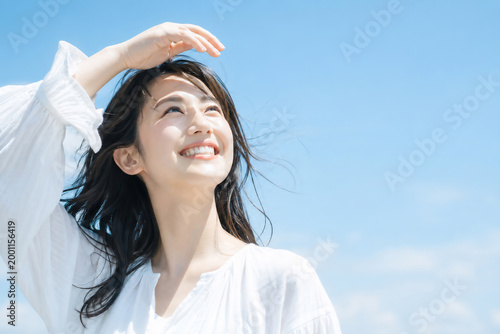 Plakat 青空の下で眩しそうに目を細め笑顔を浮かべる若い女性 紫外線対策やスキンケアのイメージ