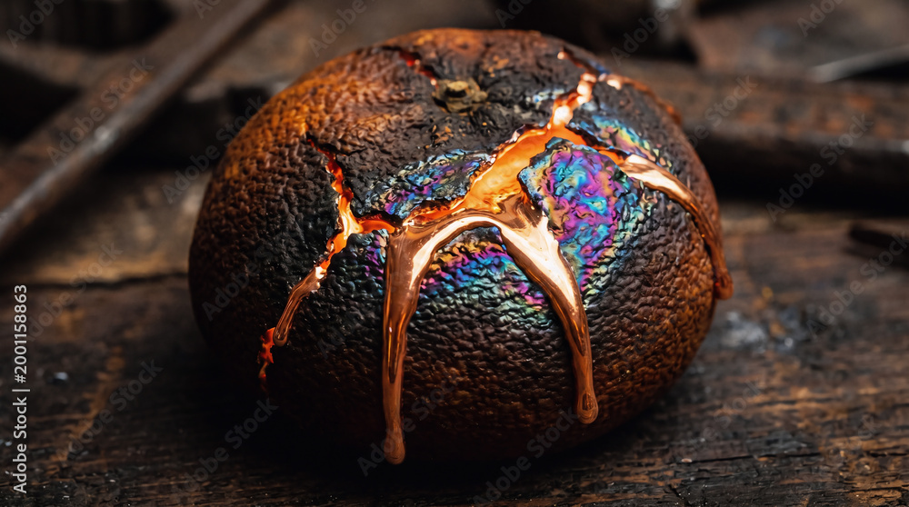Fototapeta premium A cracked and melted metal ball with a rainbow-colored surface sits on a rusty surface