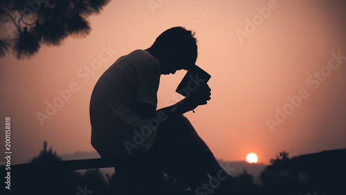 Human holding Bible and praying with light sunset background, christian silhouette concept.