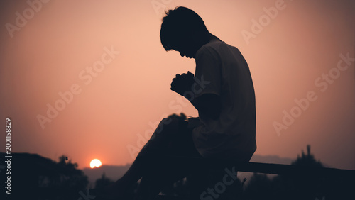 Human praying with light sunset background, christian silhouette concept.