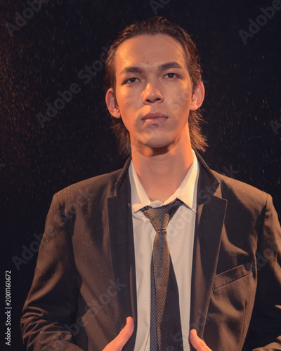 A young man in a suit stands confidently amidst falling droplets, creating an evocative portrait that reflects deep emotions, sophistication, and the essence of modern elegance.