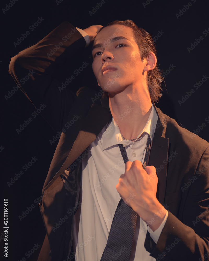 Ταπετσαρία A striking image of a young man adjusting his tie in a dramatic pose that conveys confidence and an air of mystery, with a focus on his intense expression and stylish outfit