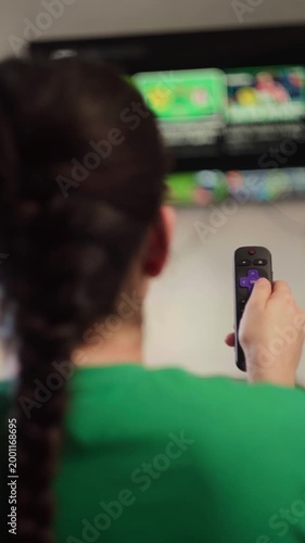 Woman with a braided ponytail holding a remote and browsing a streaming sports service on a smart tv. She navigates the user interface using the remote control buttons, watching matches of the cup