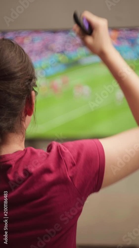 Excited woman with braided hair celebrating a goal while watching a soccer game on television and holding a remote control, expressing joy and victory at home