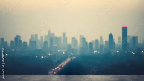 A serene and atmospheric blurry view of a metropolitan city skyline at dusk from a rooftop terrace, featuring soft bokeh lights and a hazy horizon.
