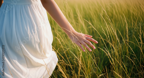 Close-up of a woman's hand touching tall grass while walking through a field at golden hour