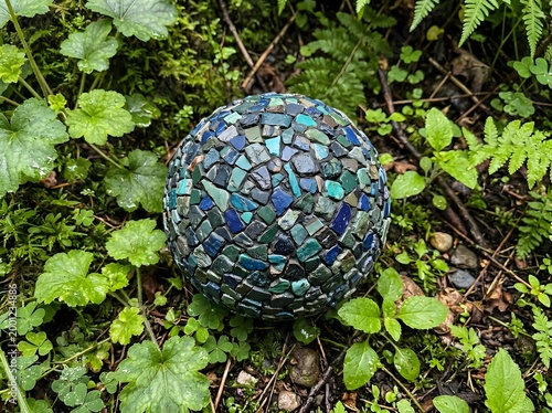 Handcrafted mosaic sphere resting in lush forest undergrowth