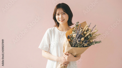 Smiling Japanese woman holding a beautiful dried flower bouquet against a pink background