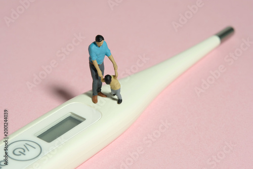 Miniature people toy figure photography. Refusing body temperature check concept. A father and son standing above thermometer. Isolated pink background