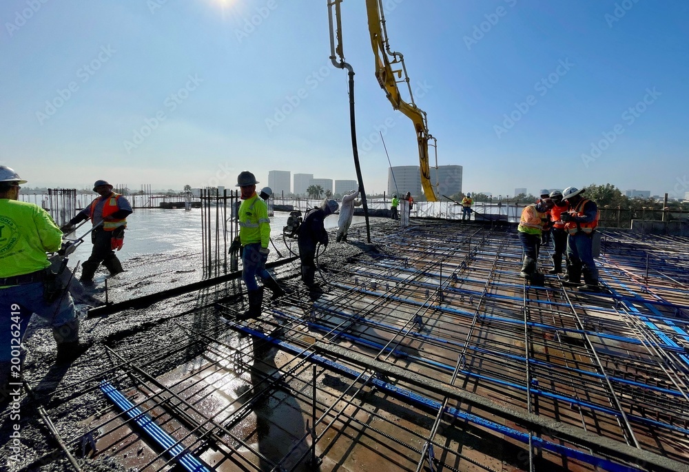 Naklejka premium Construction workers pouring concrete slab at a commercial job site