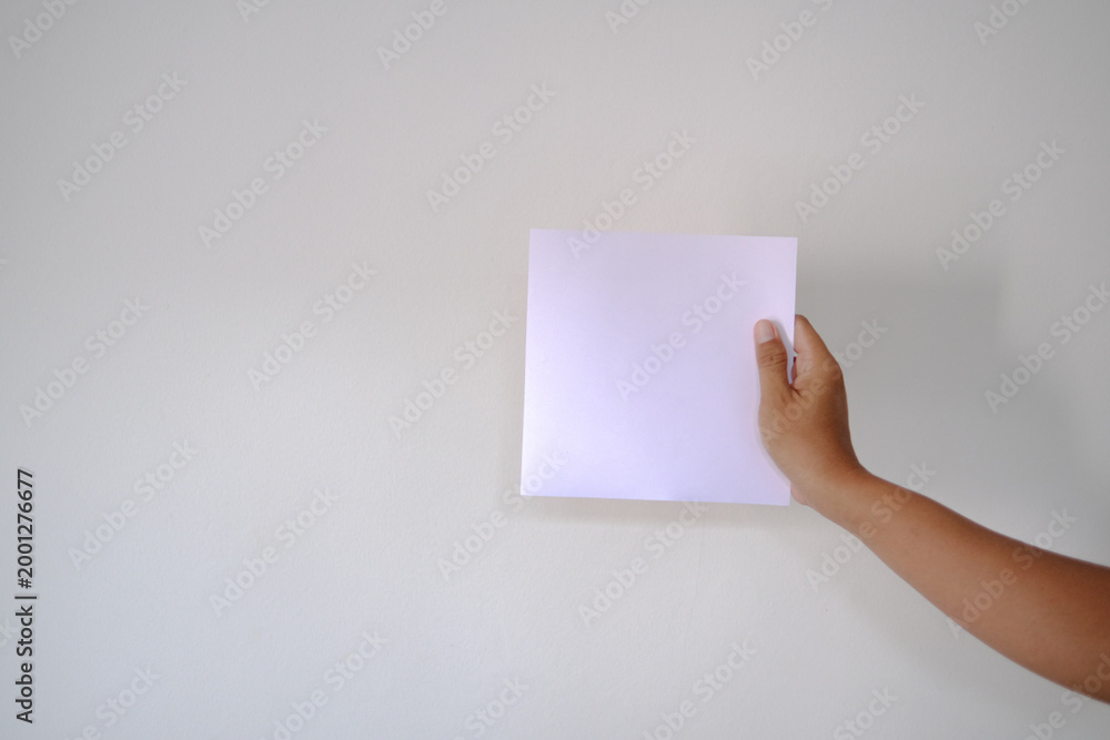 Obraz premium Holding a Blank Square of Paper Against a White Wall