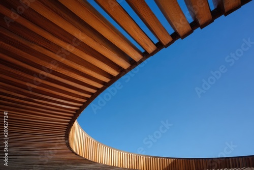 A curved wooden structure contrasts with a clear blue sky, creating a striking architectural composition.