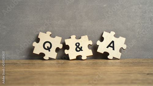 Photos Three wooden jigsaw puzzle pieces labeled Q, &, and A resting against a grey wall on a wooden surface, representing communication