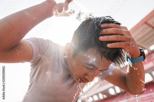 A sweaty athlete cools off by pouring water on head during hot outdoor workout session