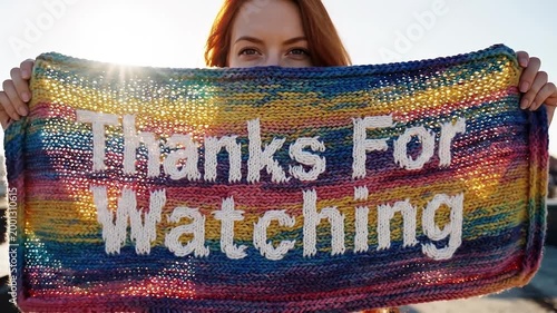 Young woman holding a knitted Thanks For Watching sign on a rooftop
