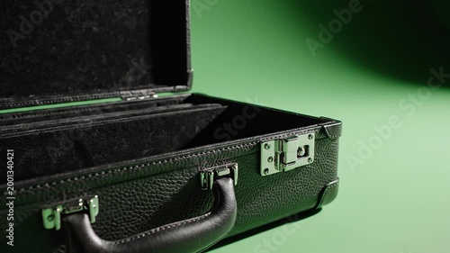 Close-up of an open black briefcase with a handle and metal latches on a green background, showcasing its interior.